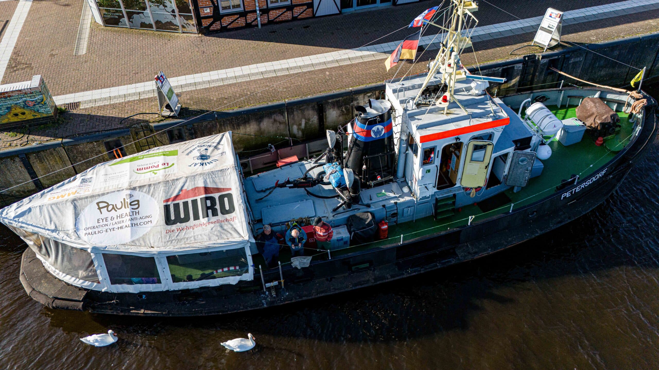 Ein Fischerboot mit Ausrüstung an Deck, schwarz-grün, schwimmt in einem ruhigen Gewässer.